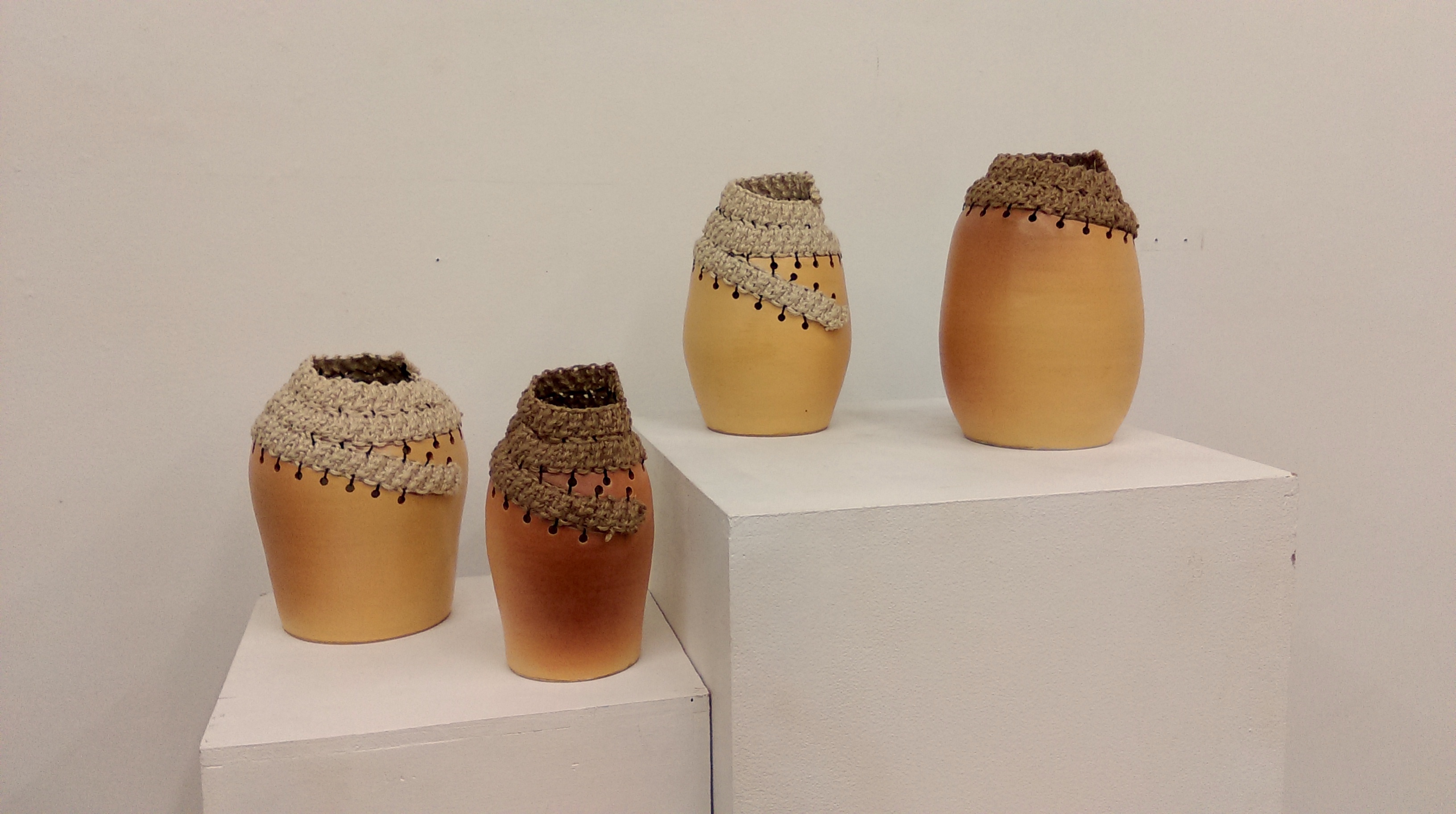 Four ceramic vessels topped with crocheted jute fiber collars
